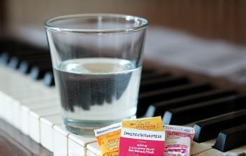 Water glass and throat lozenges on a piano keyboard, emphasizing vocal care